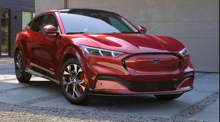 Red 2027 Ford Mustang Mach-E parked outside a modern building, highlighting its sporty electric SUV design