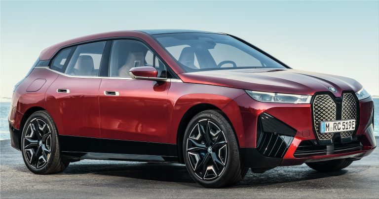 Red BMW iX electric SUV parked beside the water, showcasing its bold grille and futuristic styling