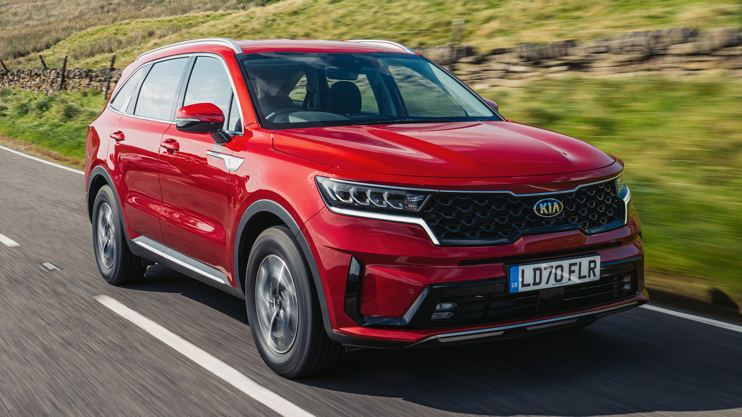 Red Kia Sorento Hybrid driving along a country road, showcasing its bold SUV styling