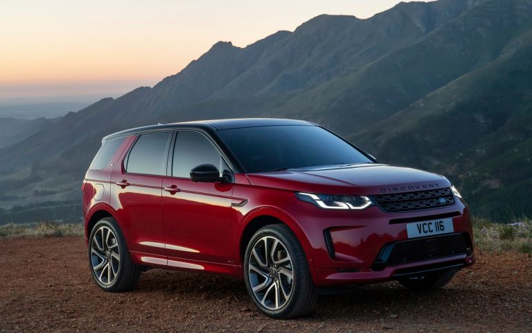 Red Land Rover Discovery Sport parked against a dramatic mountain backdrop at sunset