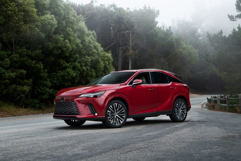 Red Lexus RX 350h parked on a quiet, misty forest road, showcasing its luxury styling