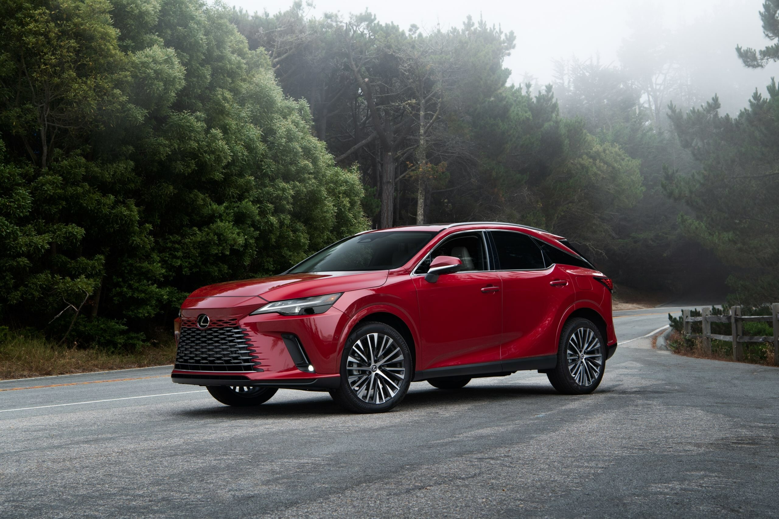 Red Lexus RX 350h parked on a quiet, misty forest road, showcasing its luxury styling