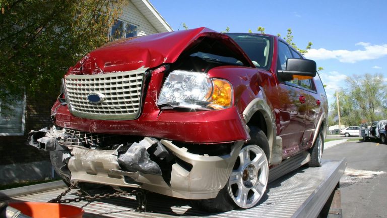 Red SUV with severe front-end collision damage secured on a flatbed recovery trailer