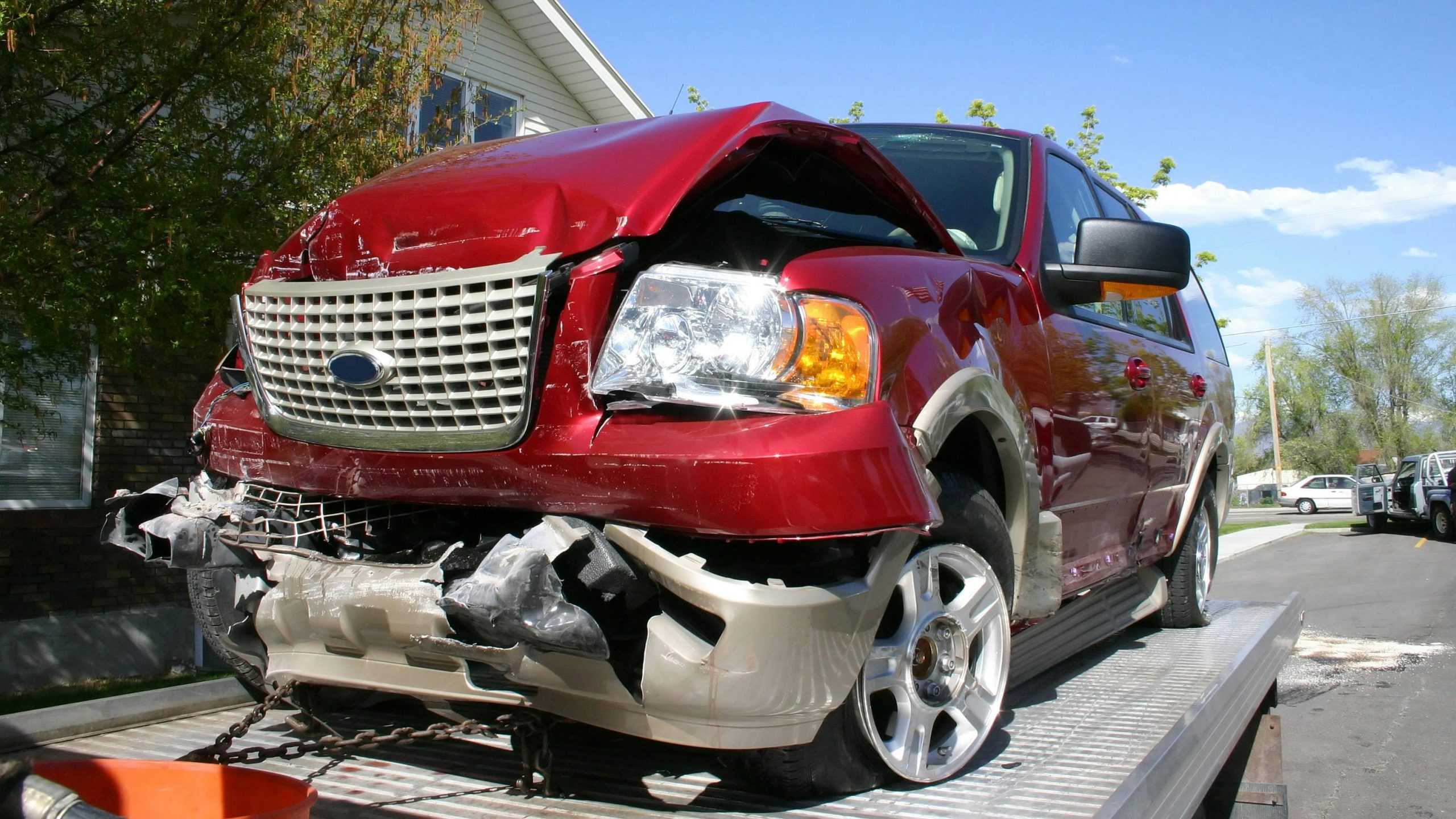 Red SUV with severe front-end collision damage secured on a flatbed recovery trailer