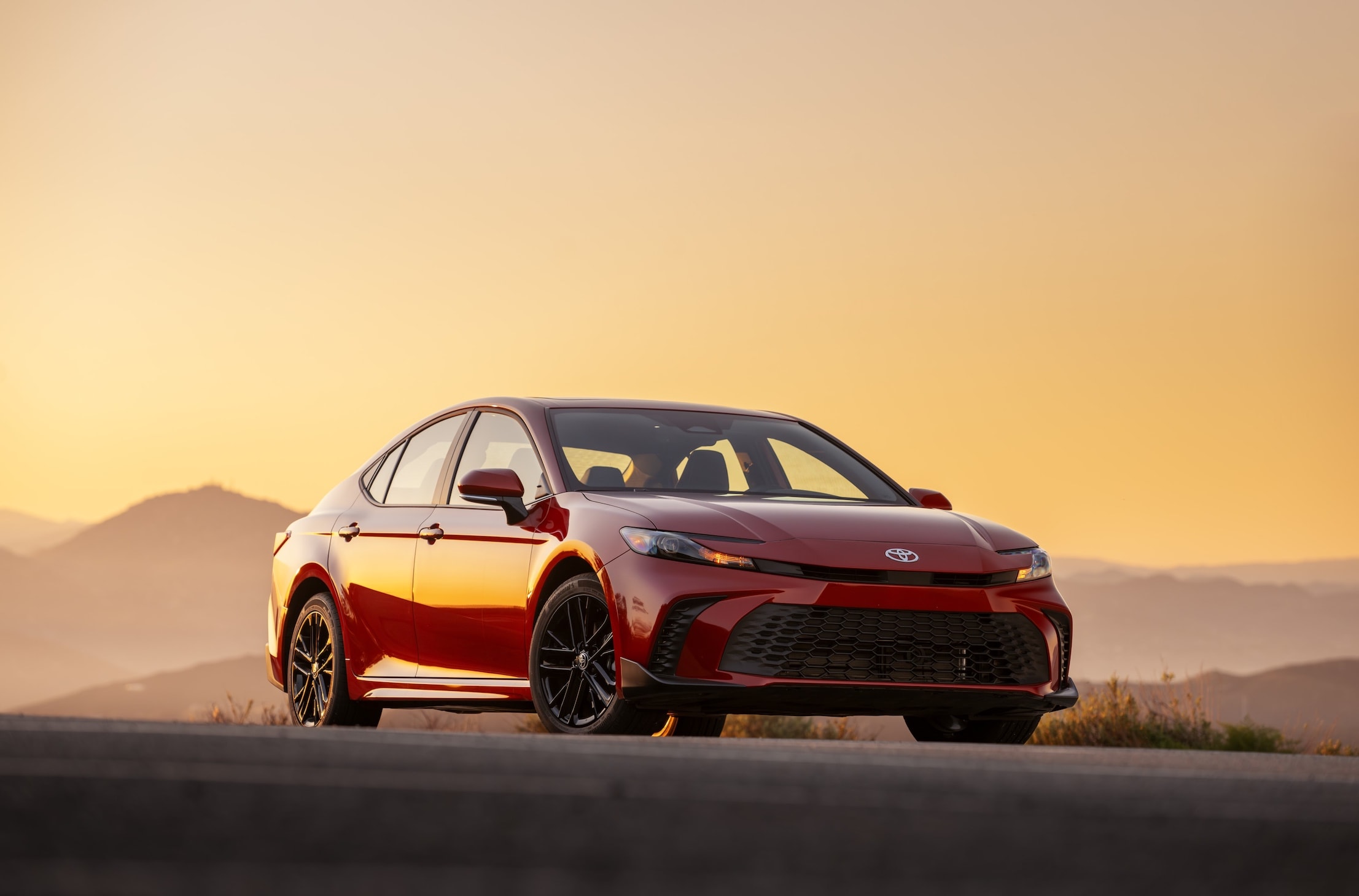 Red Toyota Camry parked against a golden sunset, showcasing its sleek design and bold front grille