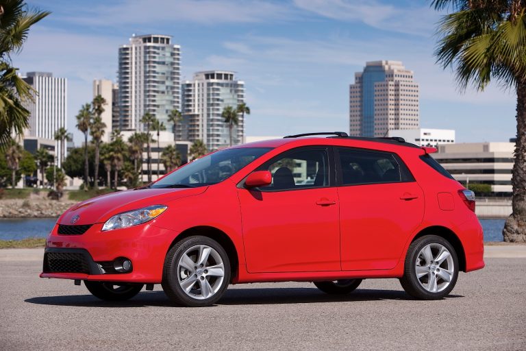 Red Toyota Matrix hatchback parked near a waterfront cityscape, highlighting its compact design and practical styling