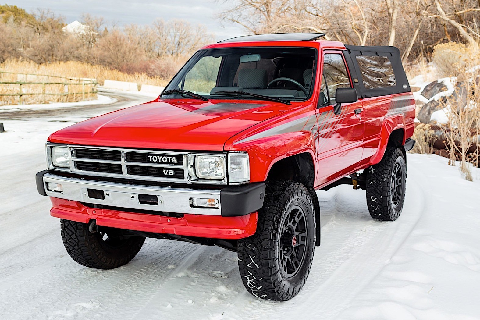 Red Toyota Pickup SR5 with lifted suspension and off-road tires parked in snow