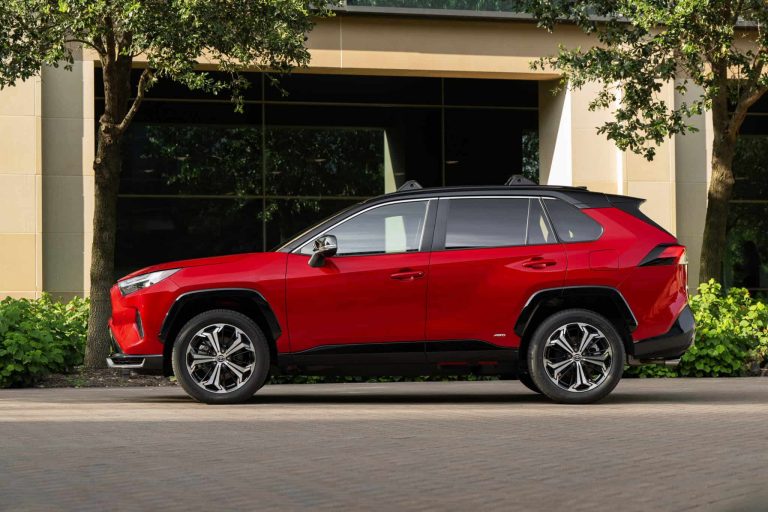 Red Toyota RAV4 Plug-In Hybrid parked outside a modern building, showcasing its sporty styling and AWD badging