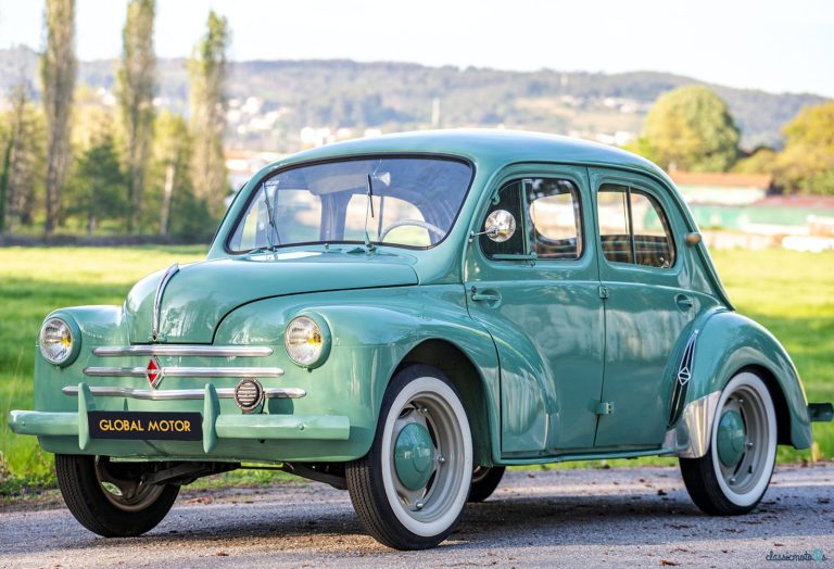 Renault 4CV parked beside a scenic countryside road with hills and greenery