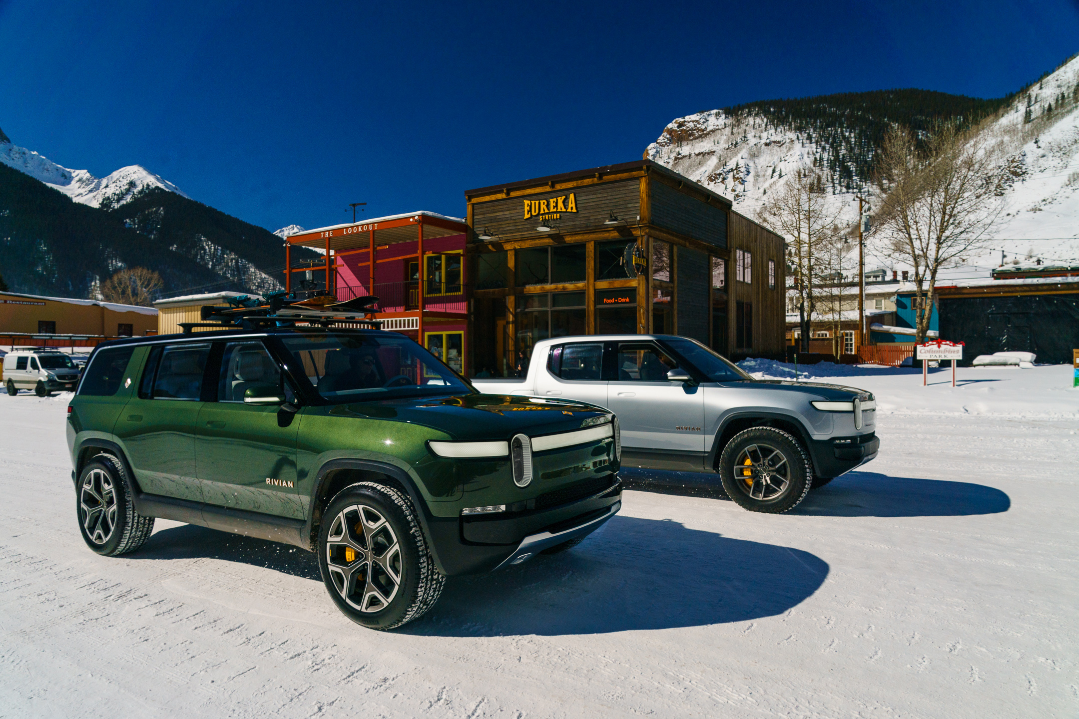 Rivian R1S SUV and R1T pickup parked in a snowy mountain town