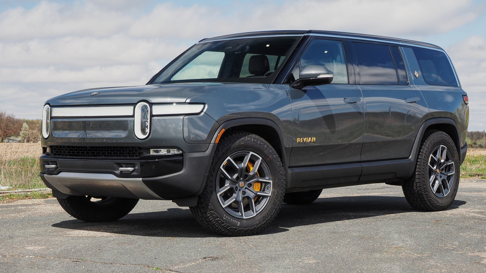 Rivian R1S SUV parked outdoors on pavement beneath a partly cloudy sky