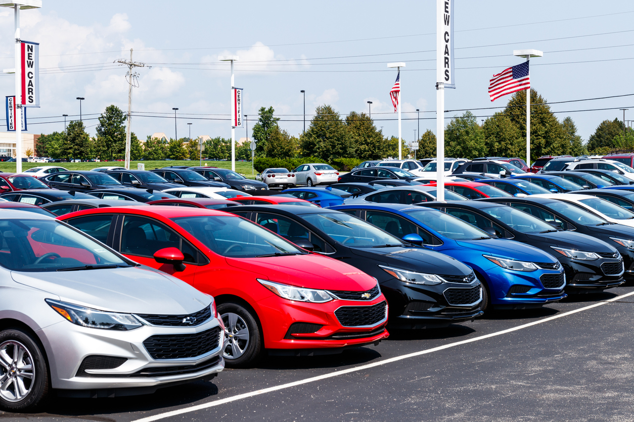 Rows of new Chevrolet sedans displayed at a dealership, with American flags flying overhead