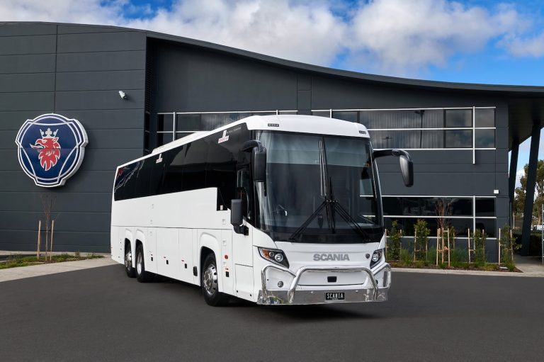 Scania Touring three-axle coach parked outside a modern commercial facility