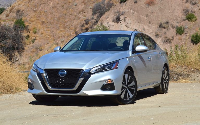 Silver Nissan Altima sedan parked on a dusty roadside against a rugged, dry hillside