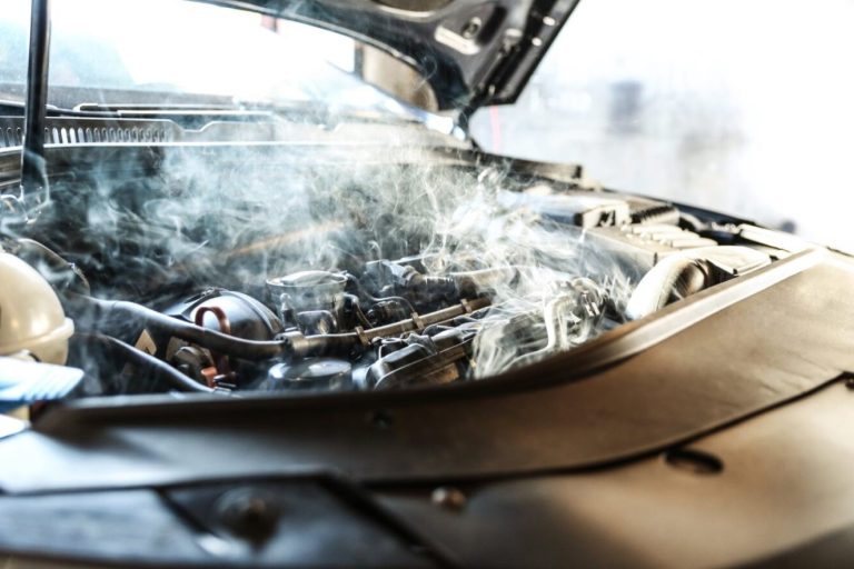 Smoke rises from a car engine compartment, indicating possible overheating or a cooling system failure