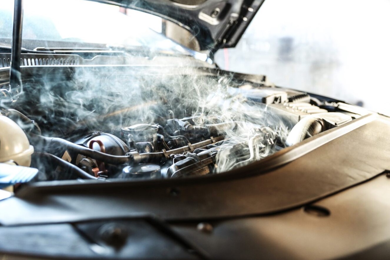 Smoke rises from a car engine compartment, indicating possible overheating or a cooling system failure