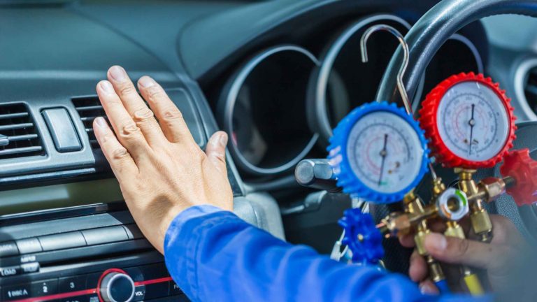 Technician checking a car’s air conditioning vents using blue and red refrigerant pressure gauges