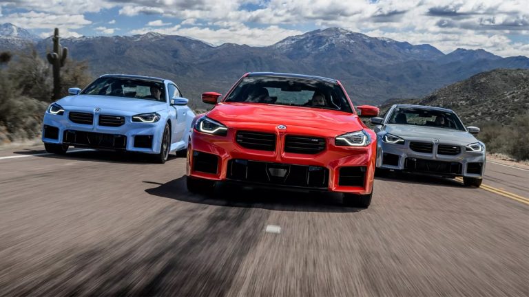 Three BMW M2 coupes, led by a red model, drive together on a mountain road