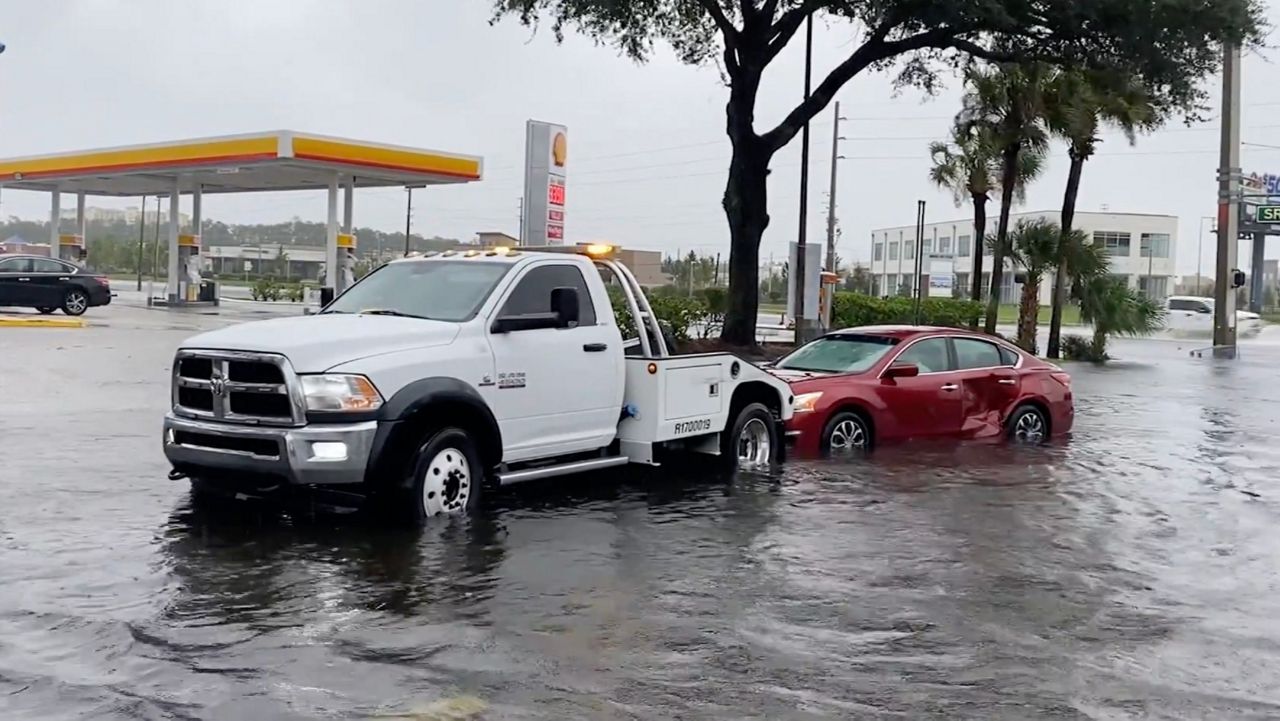 Tow truck assists a stranded red sedan stranded in deep floodwater near a gas station