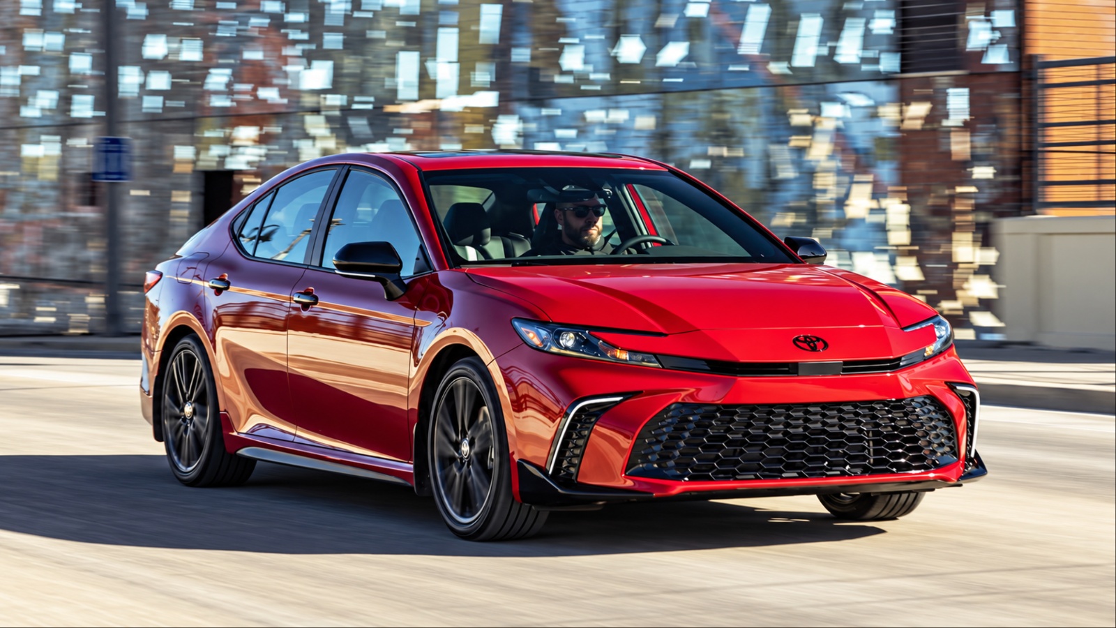 Red Toyota Camry driving on city street with male driver