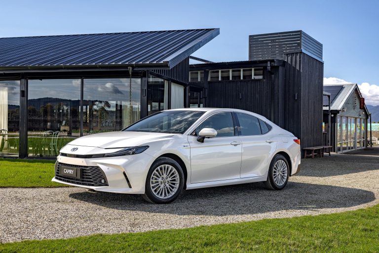 A white Camry is standing on a walk path in front of a house