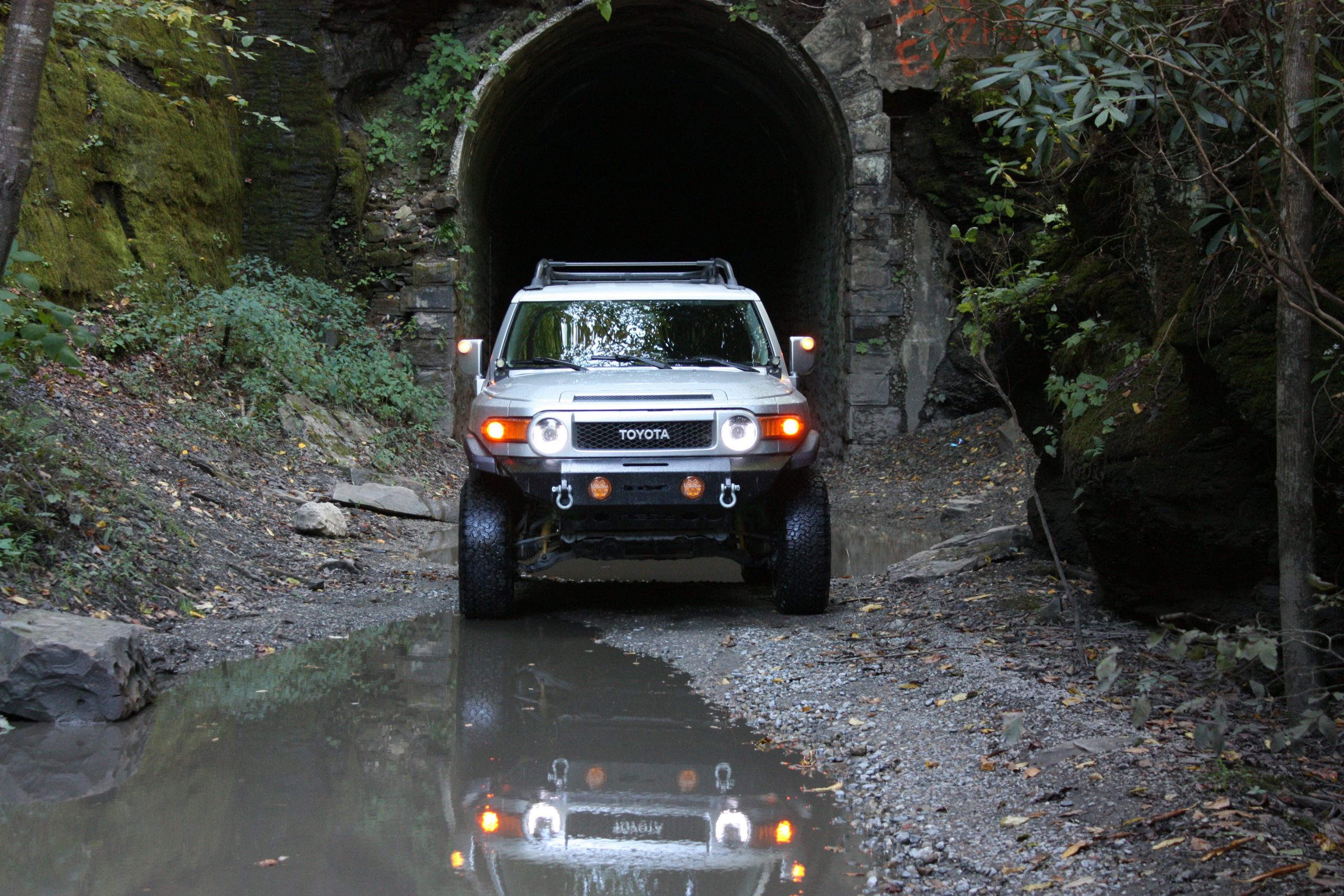 A FJ Cruiser is stanidng near muddy water in front of a cave