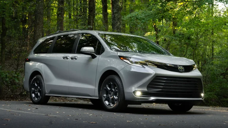 Silver Toyota Sienna Hybrid minivan parked on road in forest