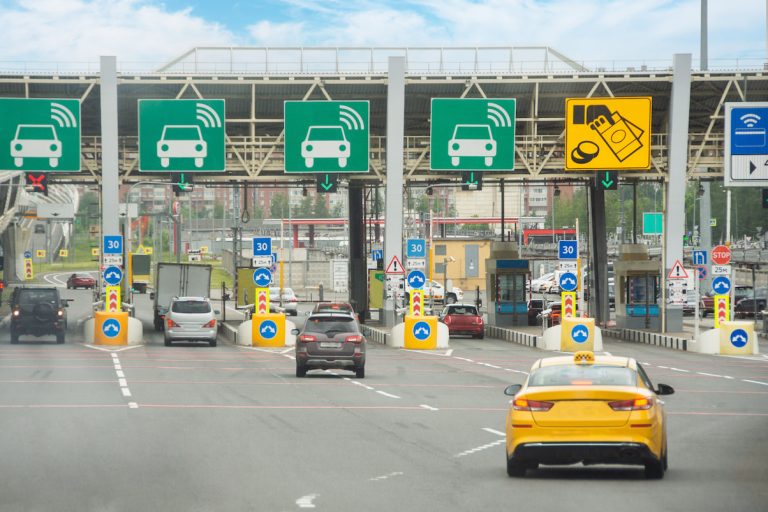 Vehicles pass through electronic toll collection lanes, with overhead transponder signs and payment indicators