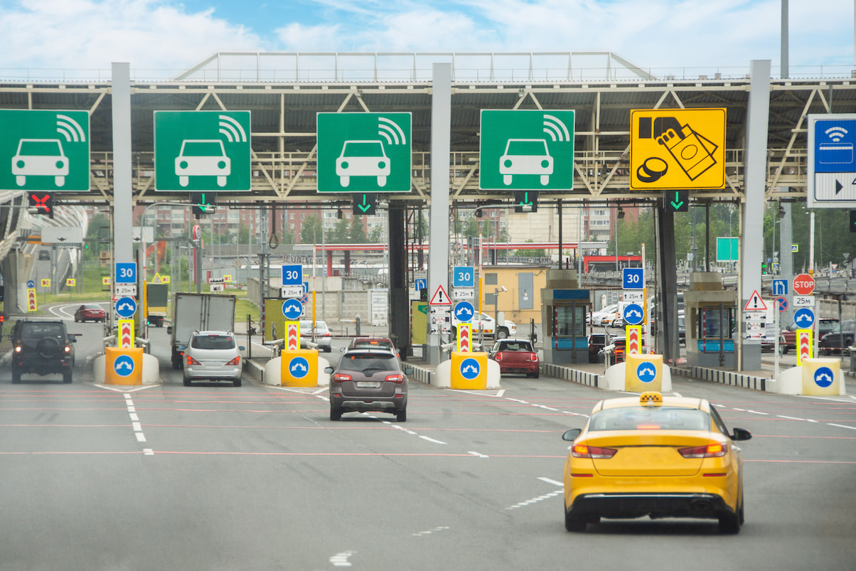 Vehicles pass through electronic toll collection lanes, with overhead transponder signs and payment indicators