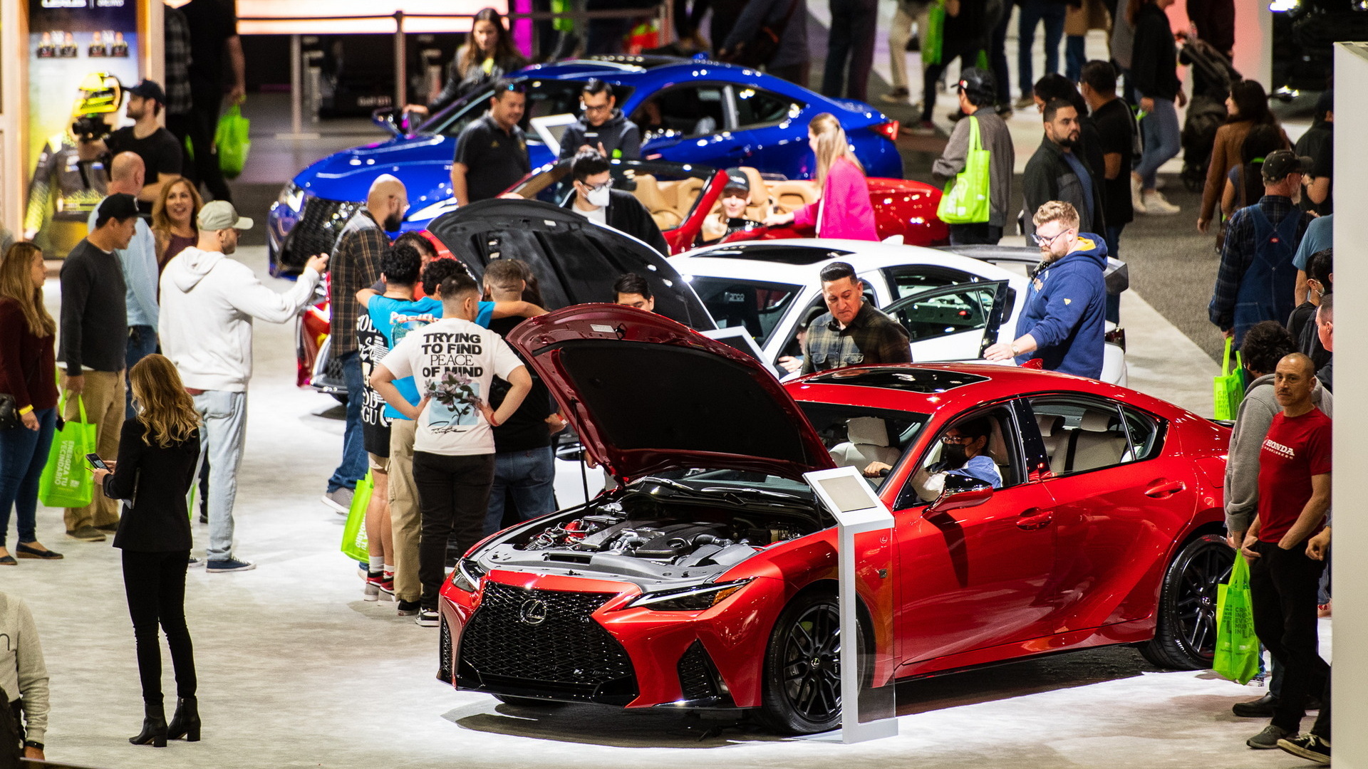 Visitors examine new vehicles at the Los Angeles Auto Show, featuring a red Lexus sedan