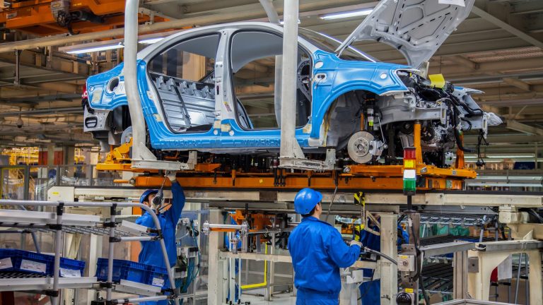 Volkswagen workers assemble a vehicle body on a busy factory production line