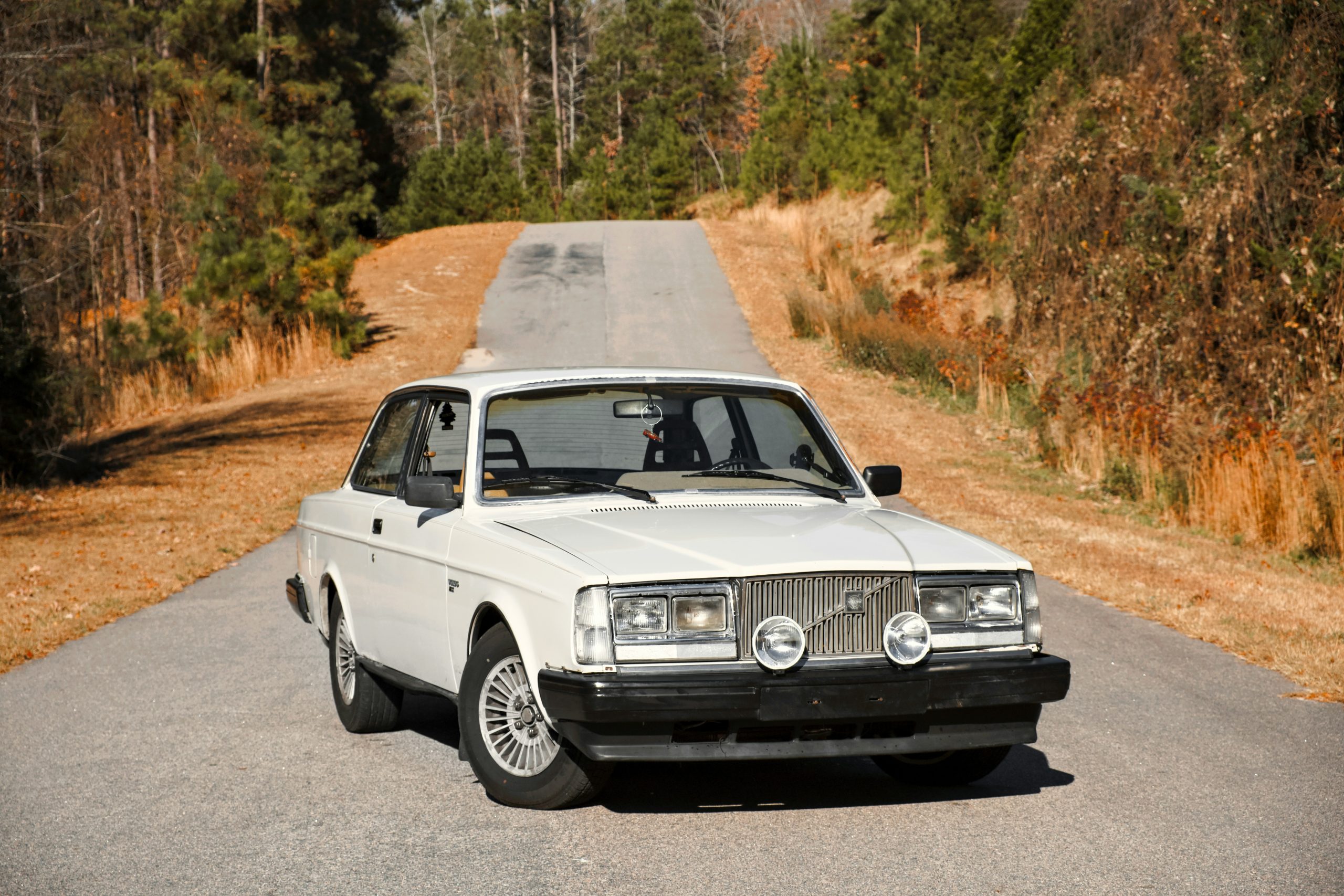 A VOLVO 240 i standing in the middle of a road on a sunny day