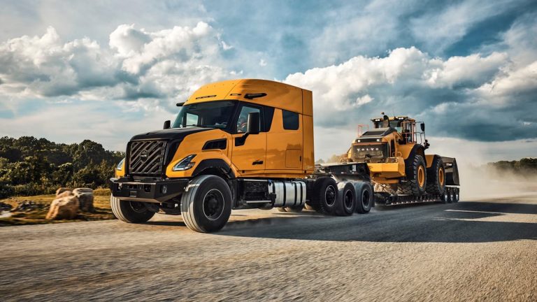 Volvo VNX heavy-duty truck transporting a large wheel loader on a trailer along a highway