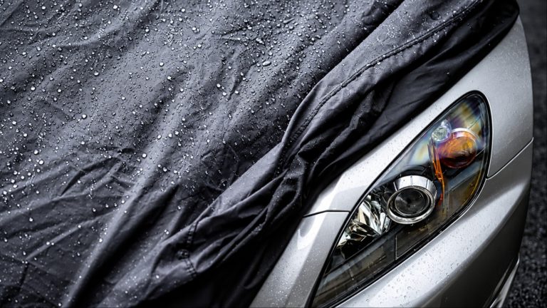 Black car cover with water droplets over silver car headlight