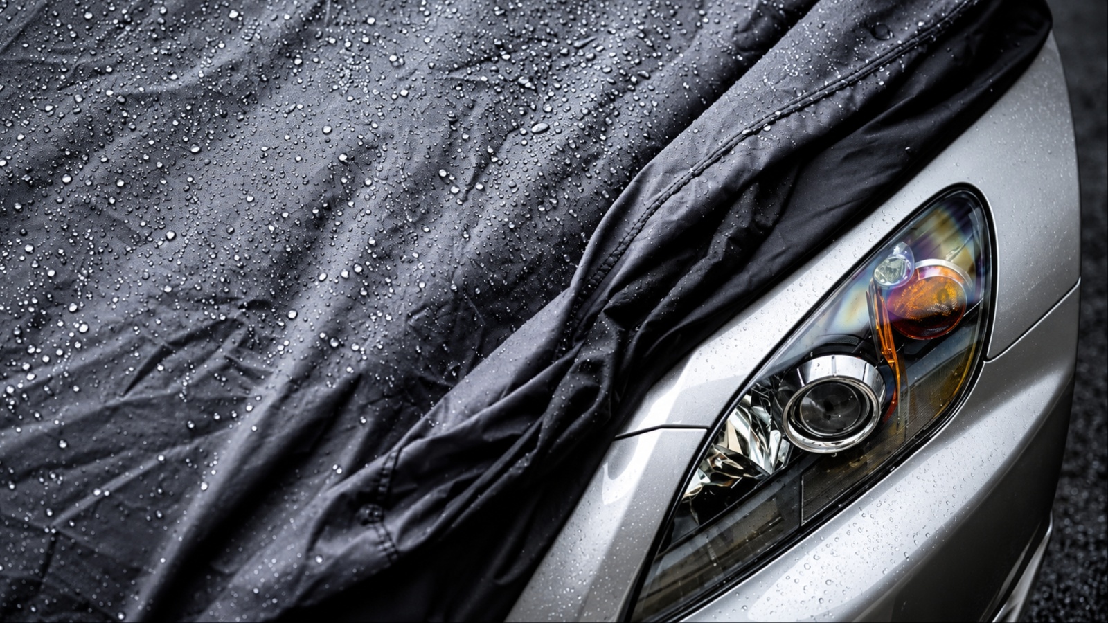 Black car cover with water droplets over silver car headlight