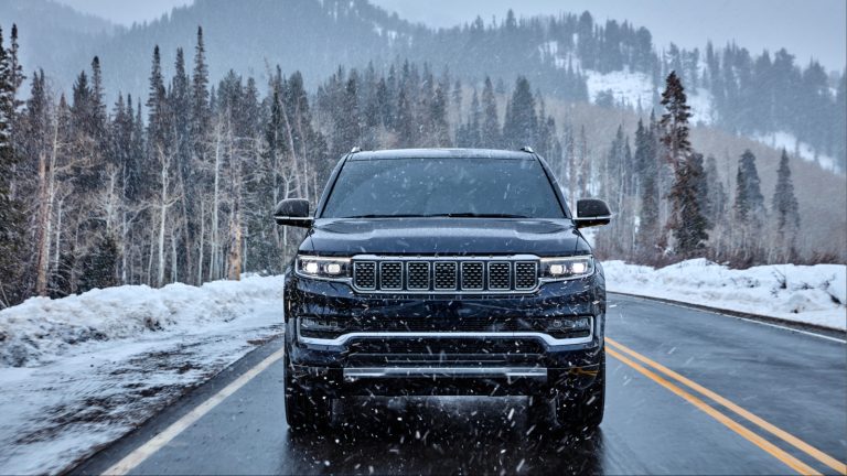 Black Jeep Wagoneer driving on snowy road through falling snow