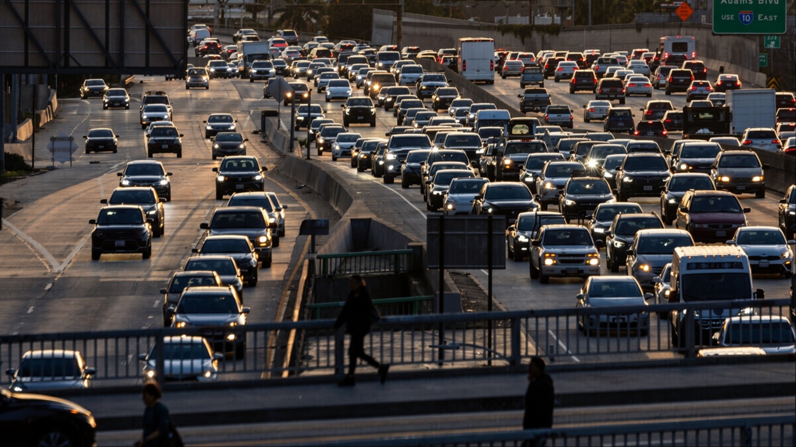 Dense traffic congestion on multi-lane highway at sunset with pedestrians