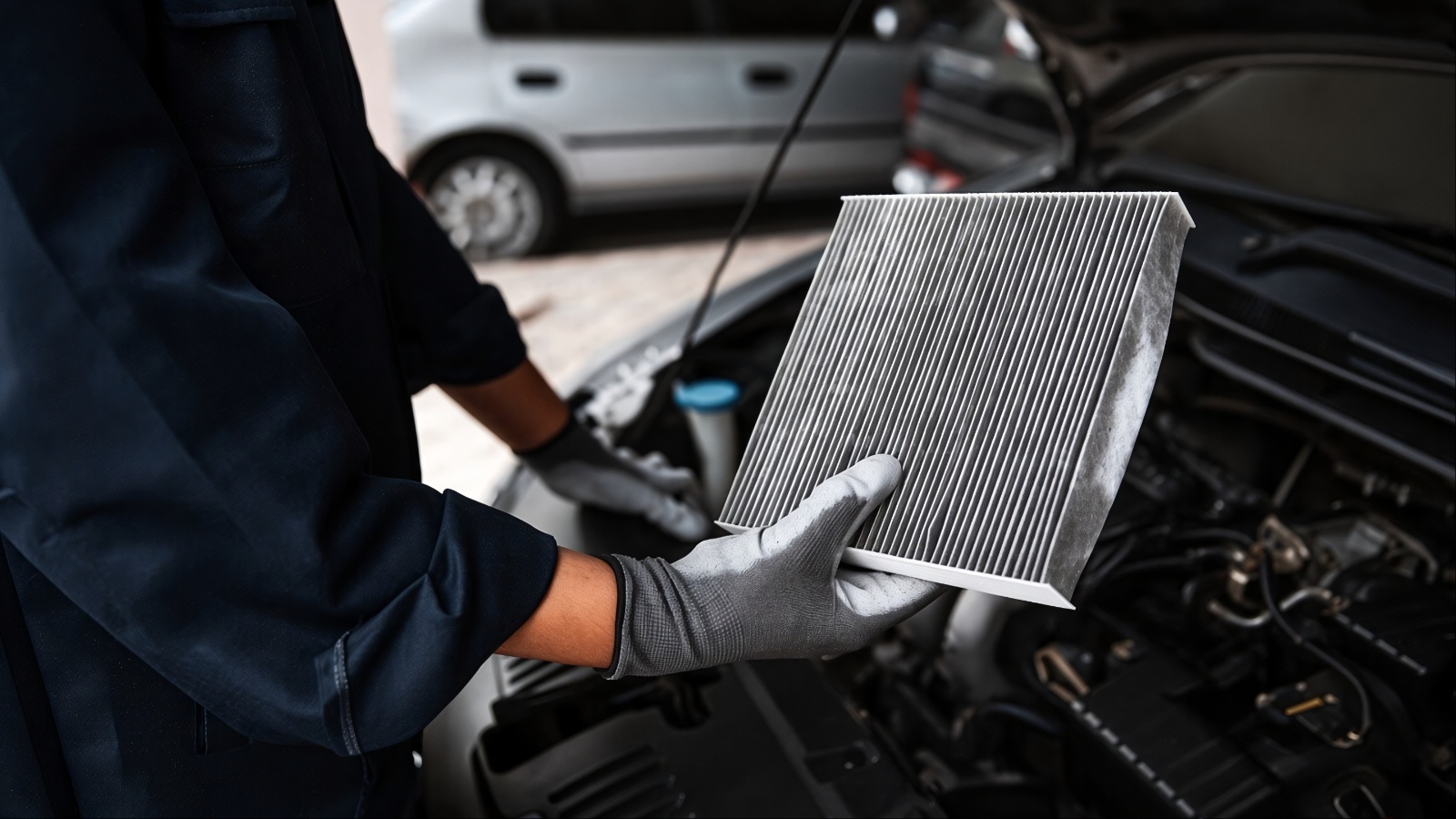 Gloved mechanic holds engine air filter near open car hood