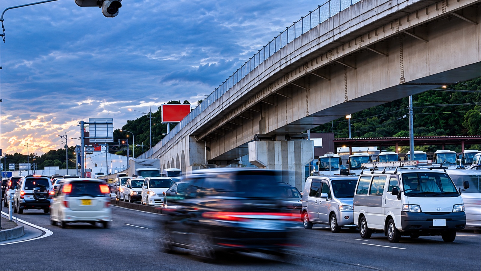 Blurred car and white vans in dusk traffic beneath elevated expressway