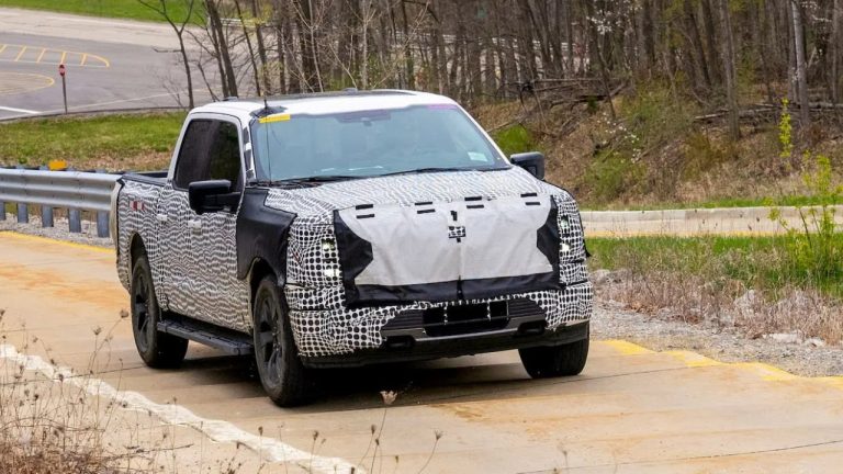 Camouflaged Ford electric pickup prototype undergoing road testing, concealing its front-end design and body details