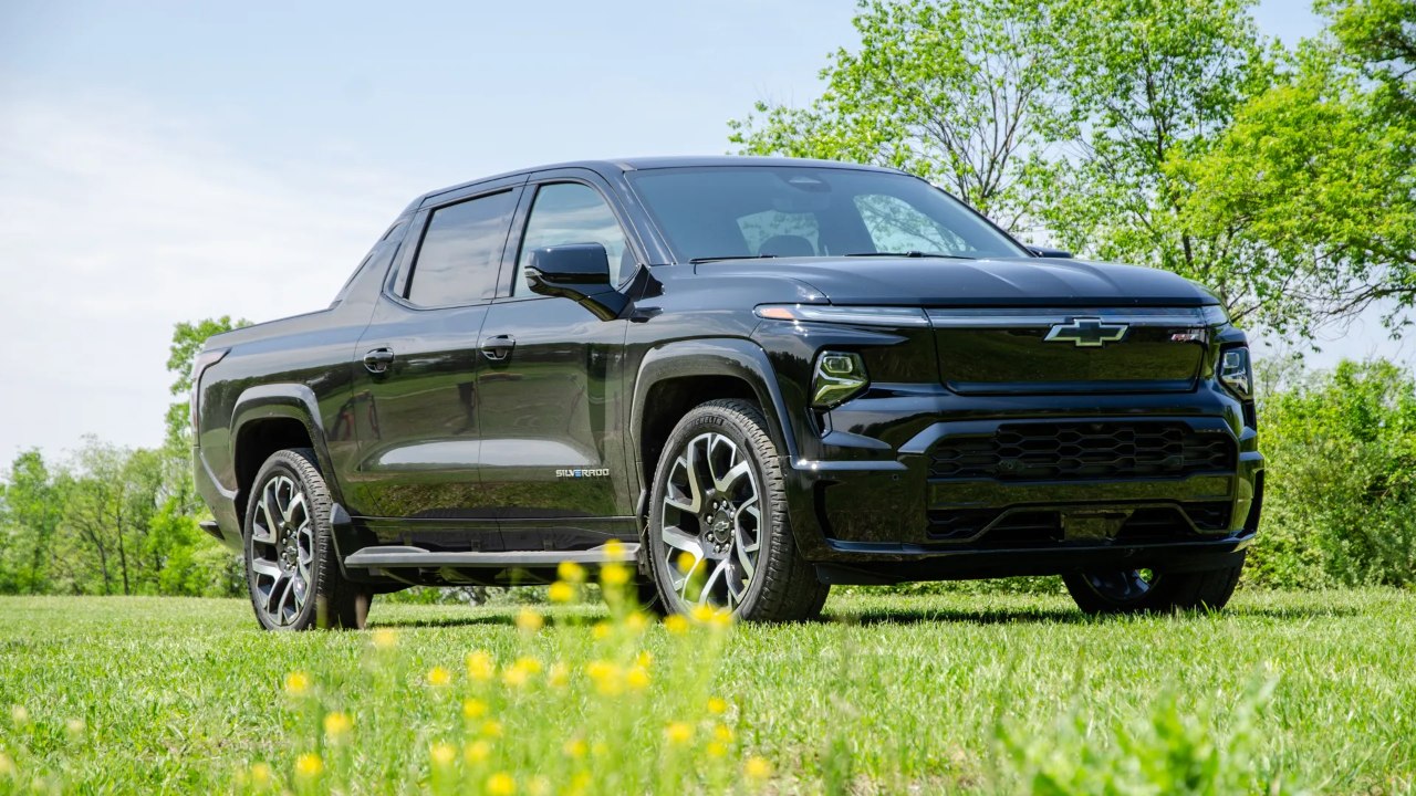 Chevrolet Silverado EV RST parked in a grassy field beneath clear skies and trees