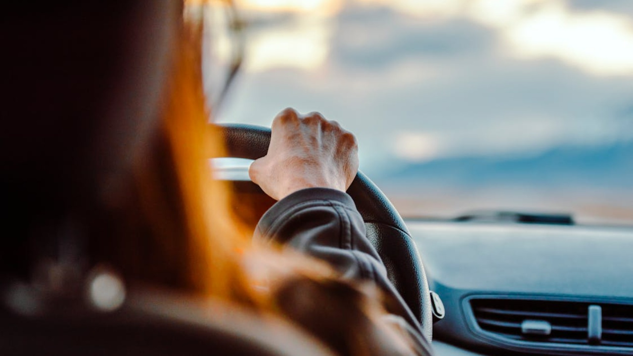 Driver holding the steering wheel while traveling along a scenic road at sunset
