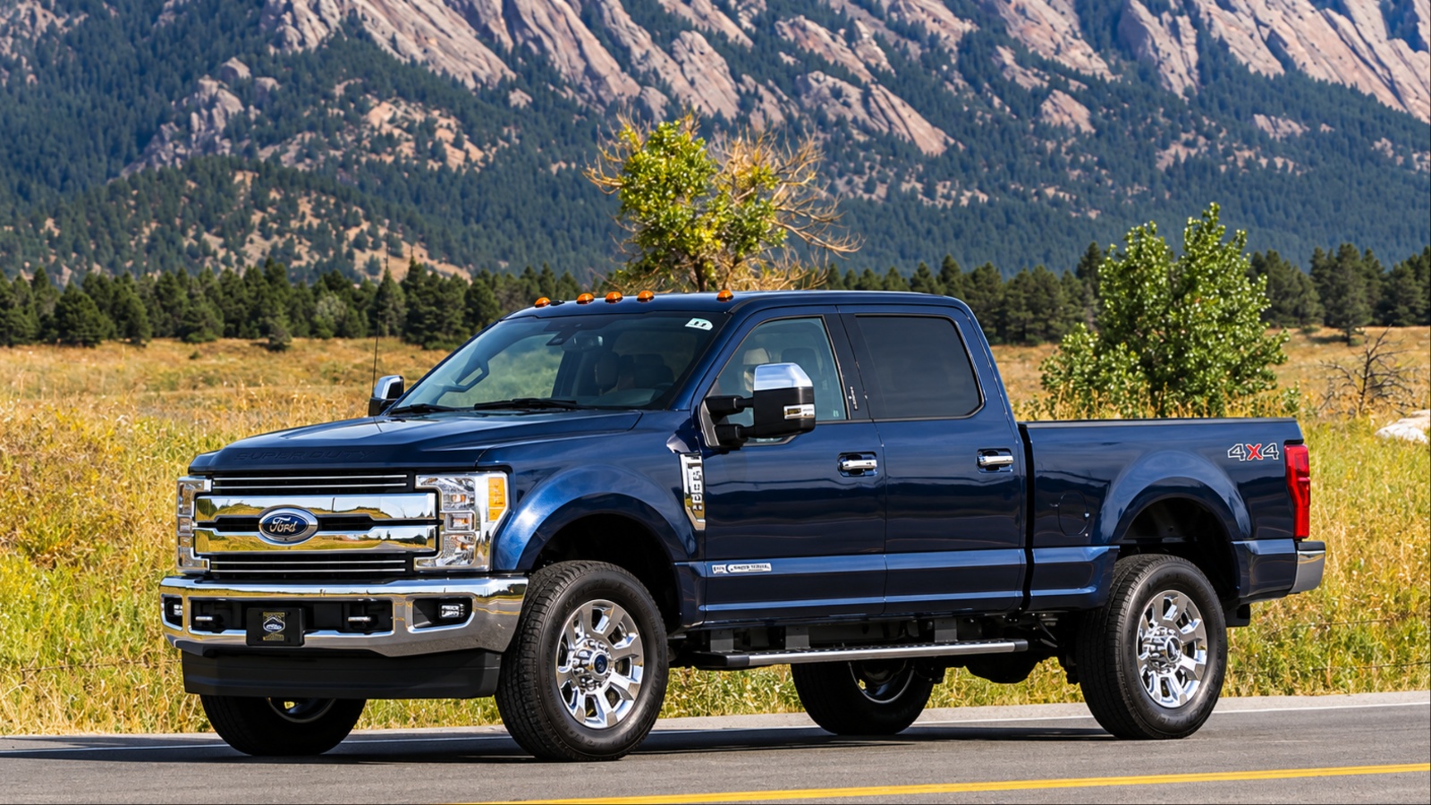Ford Super Duty pickup driving along a mountain road with rugged peaks behind