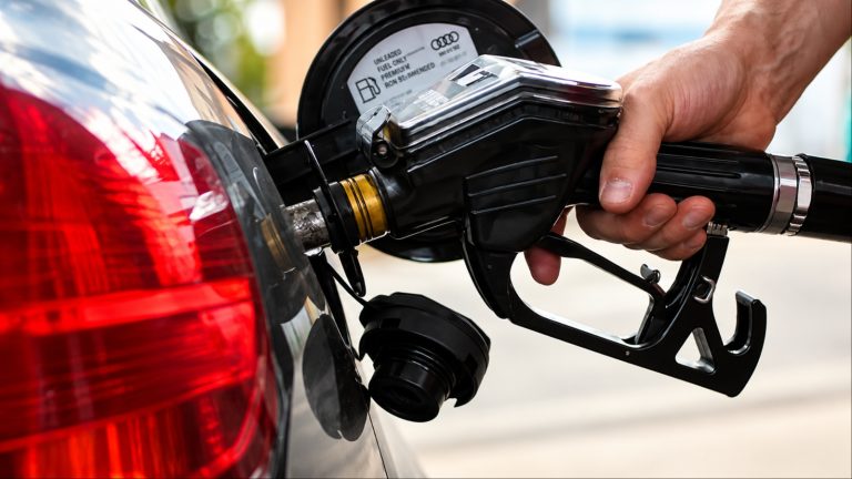 Hand gripping gas pump nozzle while refueling black sedan