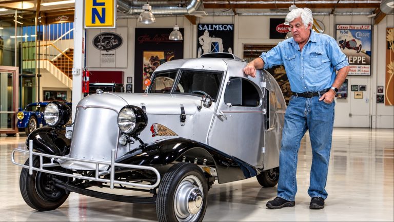 Jay Leno stands beside a vintage Indian three-wheeled car inside his automotive collection