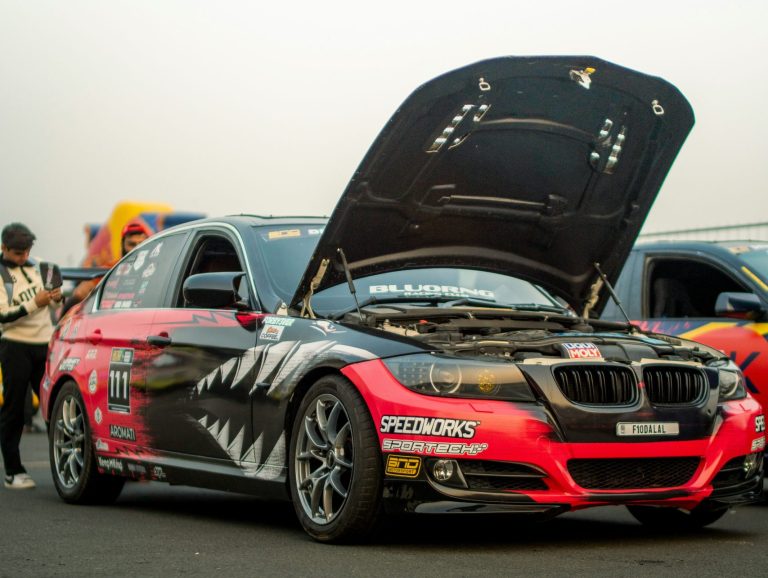 A Car is stanidng with it's hood open on a race track