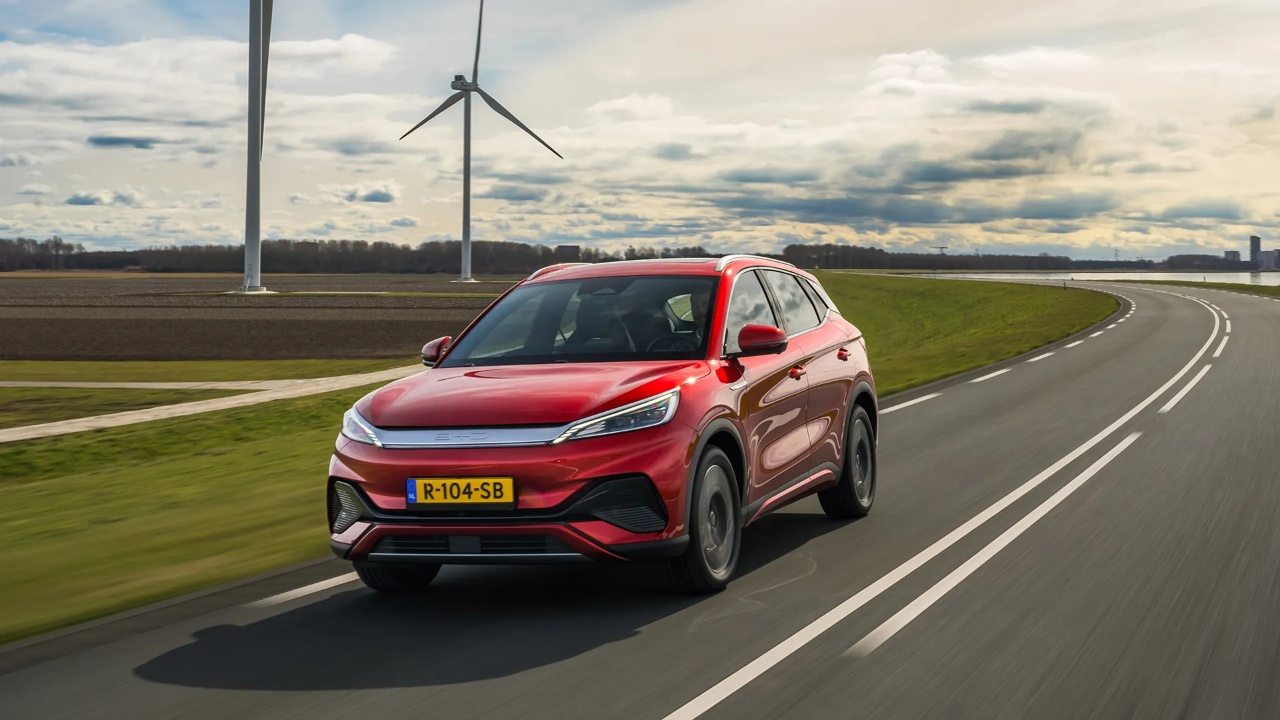 Red electric SUV drives along a curving test track beside wind turbines