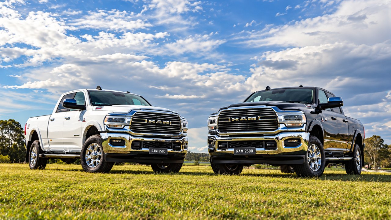 Two heavy-duty RAM 2500 pickups parked side by side on a grassy field