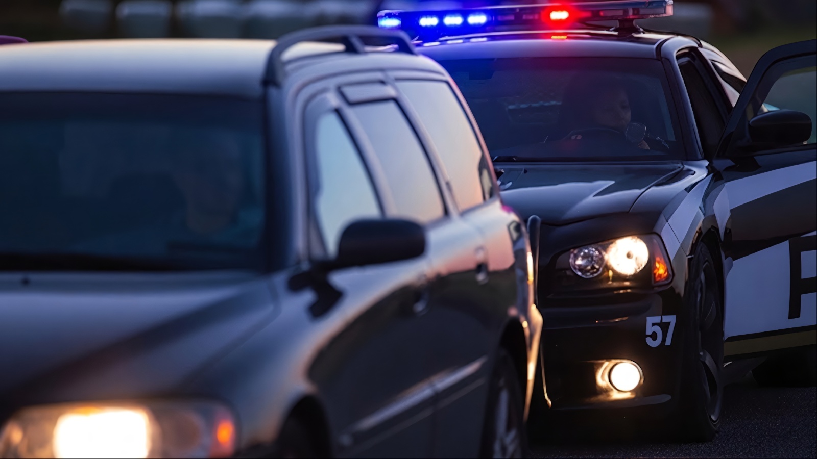 Police car with lights pulls over dark SUV at dusk