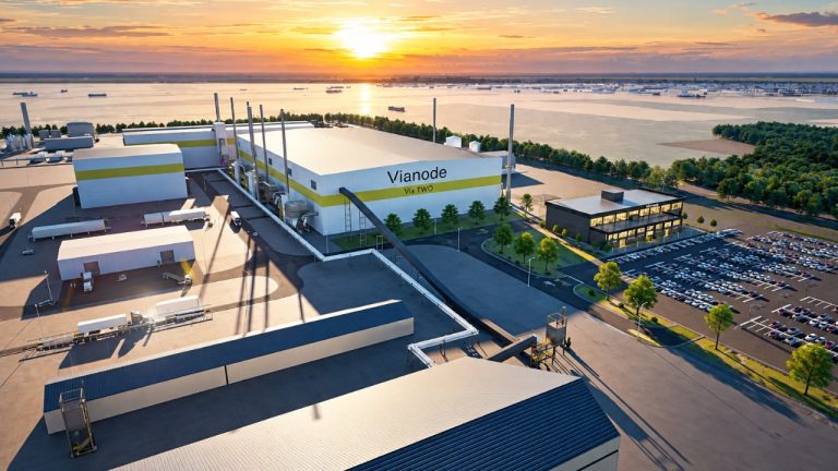 Vianode battery-material factory overlooking a waterfront industrial complex at sunset